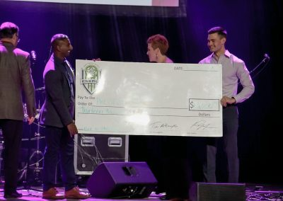 Two young men present large donation check to a man and woman on stage