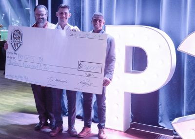 Three men take a photo while holding a large donation check