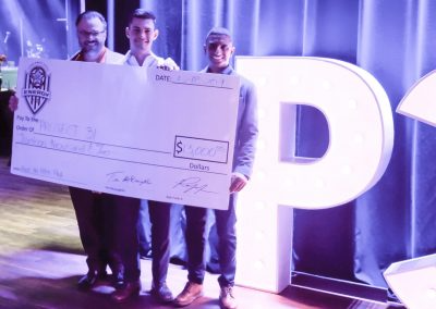 Two young men and a middle-aged man hold a large donation check