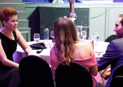 A woman with short hair sits and talks with a younger couple