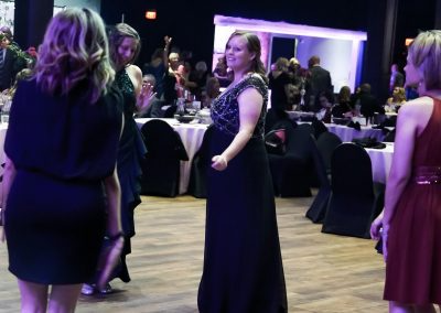 A young man woman wearing a black formal gown dances among other women