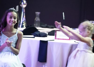 A young girl wearing a silver sparkly dress dances with a little girl wearing a pink dress