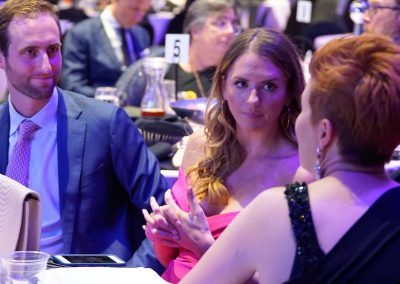 A man wearing a blue suit and a woman wearing a pink dress listed to a woman talking