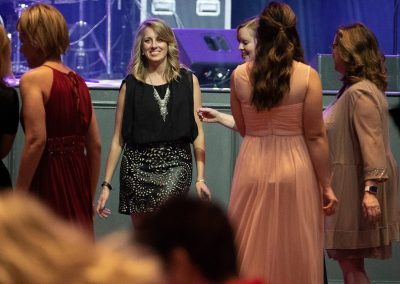 A young woman wearing a black dress smiles and walks