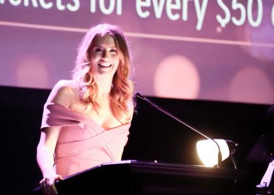 A woman wearing a pink evening gown talks at a podium at a breast cancer awareness gala.