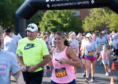 A woman wearing a pink athletic tank top runs alongside her father in a breast cancer awareness race.