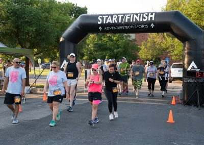 A group of adults run and walk through the finish line at a breast cancer awareness race.