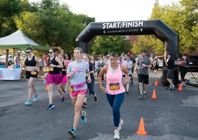 Two younger women run through the Start/Finish banner at the Pink Up the Pace race.