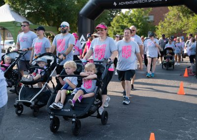 A group of adults push strollers carrying young children at. a breast cancer fundraiser race