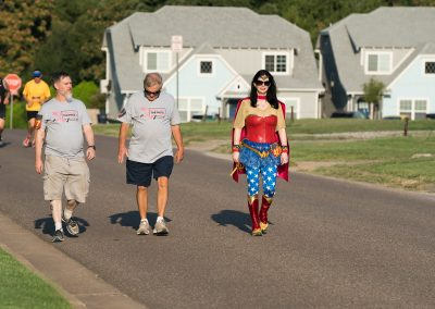 A woman dressed as Wonder Woman walks next to two men for a breast cancer fundraiser race