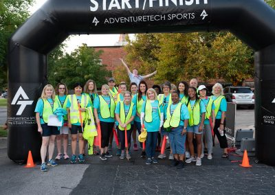 The Project31 team and a group of volunteers pose for a group photo under the Start/Finish banner. All are wearing neon yellow vests and matching blue t-shirts.