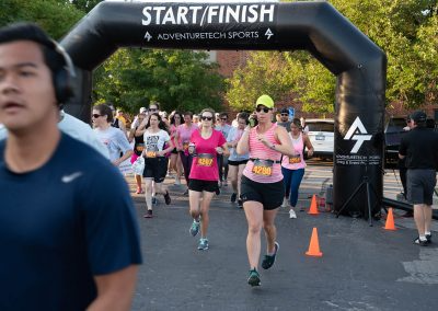 An older woman runs through the start/finish line at a breast cancer fundraiser race