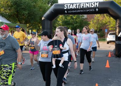 A young woman walks in a breast cancer fundraiser race while holding her baby in a carrier