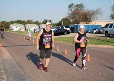 And older man and woman wearing breast cancer awareness tank tops run in fundraiser race