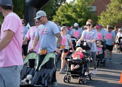 A woman pushing a stroller with two kids behind a man pushing an empty stroller at a fundraiser race