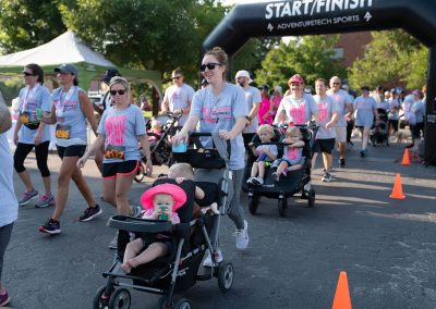 A middle-aged woman runs while pushing a strolling holding her two young children