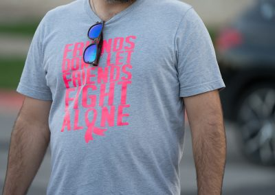 A middle-aged man wearing a grey breast cancer shirt with sunglasses hanging on the collar