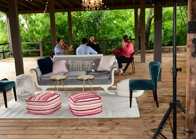 A string quartet plays together outdoors on a deck next to a grey couch and two chairs