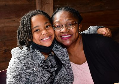 A woman with glasses smiles and hugs a young girl