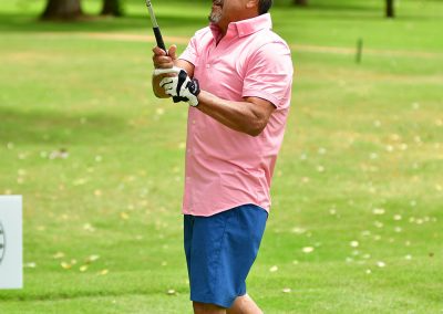 A man in a pink golf polo swings a golf club