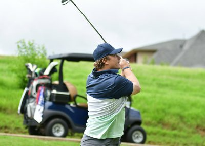 A man wearing a navy blue hat swinging a golf club