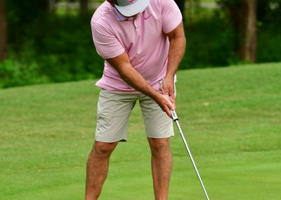 Man wearing a pink golf polo putting on the green