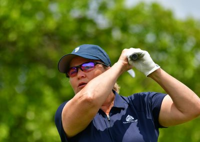 A woman wearing wearing sunglasses swings a golf club