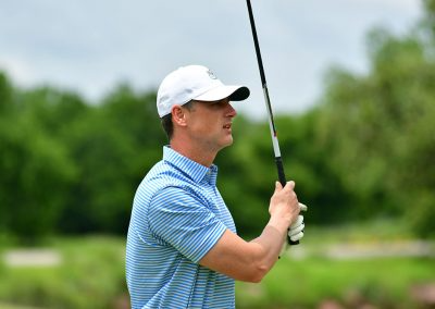 A man wearing a white hat and striped golf polo holding a glf club in the air