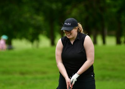 A woman wearing a black golfing tank top and black hat