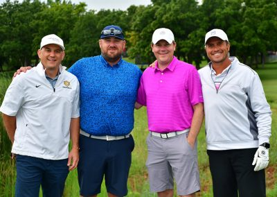 Four middle-aged men wearing hats and polos on golf course