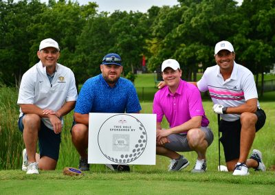 Four middle-aged men in golfing polos bend down near a sponsor sign