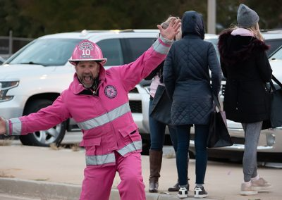 A middle-aged man wearing a pink firefighter uniform waves his hands and smiles