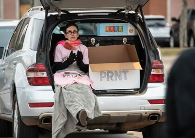 A woman with a blanket sits in the trunk of a parked car