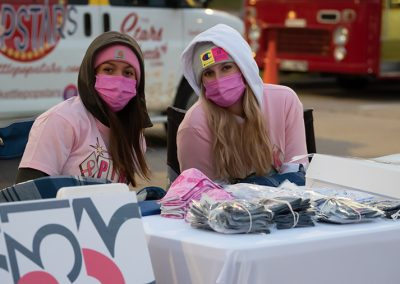 Two young women wearing pink face masks and hoodies sit at t able in the cold