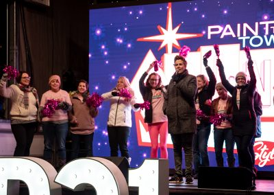 Women wave pink pom poms and cheer on stage at a breast cancer awareness event