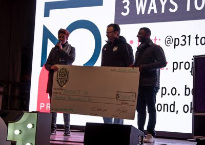 A middle-aged woman holds a large donation check with two men