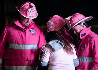 A woman talks to three men wearing pink firefighter uniforms