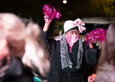 A woman wearing a black coat waves pink pom poms in the air