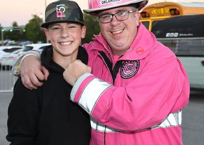 Middle-aged man in pink firefighter uniform hugging a teenage boy with a camo hat
