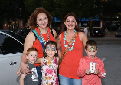 Three young kids wearing face paint smile for a photo with two young women wearing orange tank tops