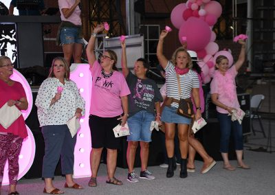 A group of women wearing pink ring bells and cheer at a breast cancer awareness event