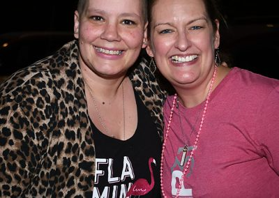A young woman wearing a leopard cardigan smiles with a middle-aged woman wearing a pink breast cancer t-shirt