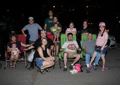 A group of adults and children sit in lawn chairs outside at night