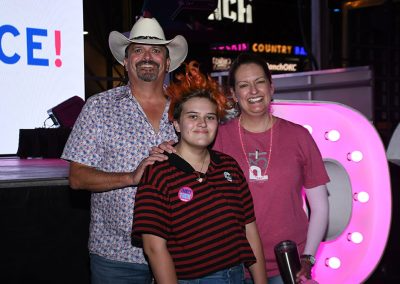 A teenage girl wearing a striped shirt smiles and stands in front of her mother and father