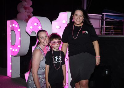 Two young women smile for a photo with a young boy wearing large pink sunglasses