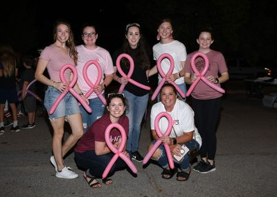 A group of young women hold pink balloons shaped like breast cancer ribbons