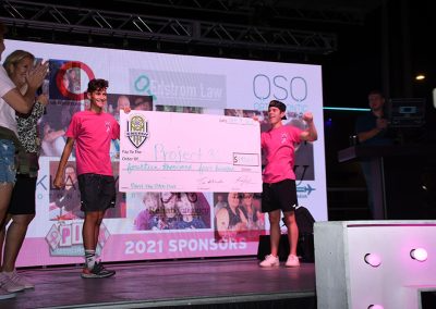 Two teenage boys hold a large donation check on stage