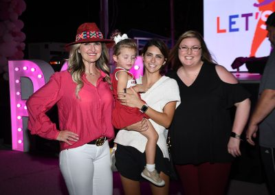 Three young women smile for a photo as the woman in the middle holds a young girl.