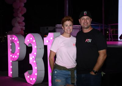 A woman with short red hair takes a photo with her husband in front of a large lighted sign