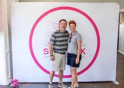 A woman with short red hair smiles for a photo with an older man in a striped polo shirt